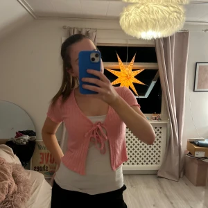 Rosa kortärmad bolerotopp - Söt rosa bolerotopp med korta ärmar och knytning framtill. Perfekt för att lägga till en färgglad touch till din outfit.