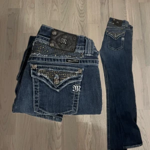 Blå jeans från Miss Me - Snygga blå jeans från Miss Me med dekorativa detaljer och broderier på bakfickorna. Jeansen har en klassisk femficksdesign och är prydda med nitar och mönster. Perfekta för dig som vill ha något unikt i garderoben!