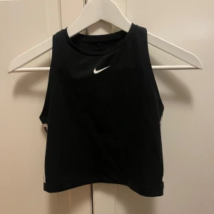 Svart linnetopp från Nike - Snygg svart linnetopp från Nike med vit logga framtill. Perfekt för träning eller en sportig look. Tillverkad i ett bekvämt material som andas.