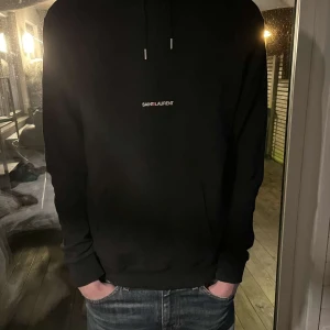 Svart hoodie från Saint Laurent - Snygg svart hoodie från Saint Laurent med logotyp på bröstet. Perfekt för en stilren och avslappnad look. Den har långa ärmar och en klassisk huva med dragsko.