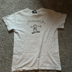 Vit t-shirt från Thrasher - Säljer en vit t-shirt från Thrasher med ett coolt tryck av en skateboardåkare på framsidan.  T-shirten har en klassisk passform och korta ärmar.
