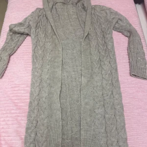 Beige stickad kofta med huva - Mysig beige stickad kofta med huva och kabelstickat mönster. Perfekt för kyliga dagar och ger en avslappnad look. Långärmad design som passar bra till lager-på-lager-stil.