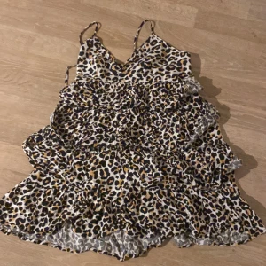Leopardmönstrad klänning med volanger - Trendig leopardmönstrad klänning med volanger och smala axelband. Perfekt för en djärv look med sin v-ringade design.