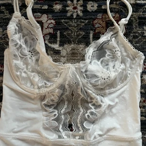 Vit spetsbody från Kappahl! - Säljer en elegant vit body från Kappahl med vackra spetsdetaljer och justerbara axelband. Endast testat, så i nyskick! Köptes för cirka 450kr. Bodyn har en fin prickig struktur och spetsen pryder både fram- och baksidan. 