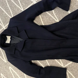 Marinblå kappa  - Säljer en stilren marinblå kappa från ONLY i storlek S. Perfekt för höst och vinter med sin klassiska design och långa ärmar. Kappan är i väldigt bra skick. Perfekt i längden också.