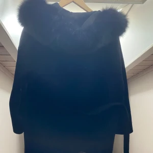 Svart pälsjacka med huva (Äkta päls) - Säljer en elegant svart pälsjacka med fluffig huva. Perfekt för kyliga dagar när du vill hålla dig varm och stilren. Jackan har en klassisk design och är supermjuk att ha på sig. Passar perfekt till både vardag och fest!
