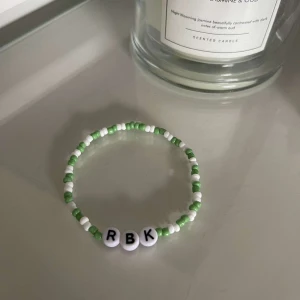 Pärlarmband med bokstäver - Ett supergulligt armband med gröna och vita pärlor. Det har tre vita bokstavspärlor som bildar 'RBK'. Perfekt för att ge en personlig touch till din stil!