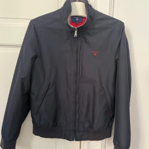 Höst- och vårjacka från Gant - Snygg mörkblå höst- och vårjacka från Gant med rött foder.  Jackan är i bra skick!  Fler bilder kan skickas om så önskas. 