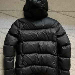 Gant vinterjacka dun svart - Tjock svart dunjacka frpn Gant i croppad modell. Slitning insida dragkedja men inget som syns eller påverkar funktion. Jackan kan stängas som vanligt.