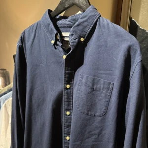 GAP SKJORTA - En riktigt snygg marinblå skjorta från GAP med vita knappar och en bröstficka. Går att använda till vardagen men även till finare tillfällen. Den är mycket stilren och fungerar till alla årstider. Nästintill nyskick, ordinarie pris 500