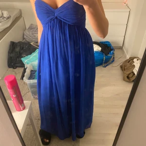 Blå axelbandslös långklänning - Snygg blå axelbandslös långklänning med en elegant drapering över bysten. Perfekt för sommarens festligheter. Klänningen har en smickrande passform och är tillverkad i ett mjukt och följsamt material.
