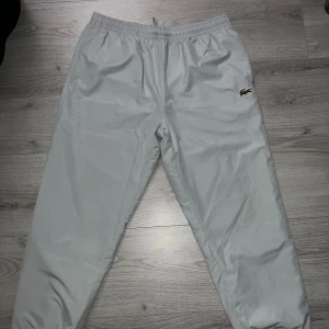 Lacoste byxor - Lacoste träningsbyxor, storlek 6 / XL. Tunna luftiga byxor från Lacoste med speciell brun/röd krokodil logga.