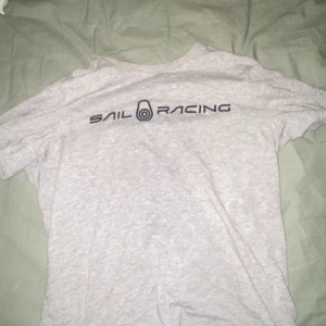 Grå t-shirt från Sail Racing - Snygg grå t-shirt från Sail Racing med tryck på bröstet. Perfekt för en avslappnad stil. T-shirten har en klassisk passform och är kortärmad.