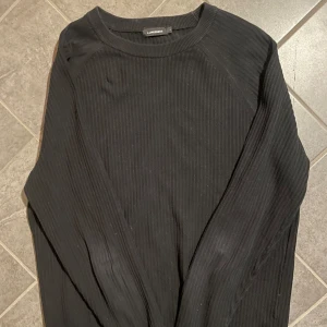 Svart ribbad tröja från J.Lindeberg - Säljer en stilren svart ribbad tröja från J.Lindeberg. Tröjan har långa ärmar och en klassisk rund halsringning. Perfekt för en minimalistisk look.