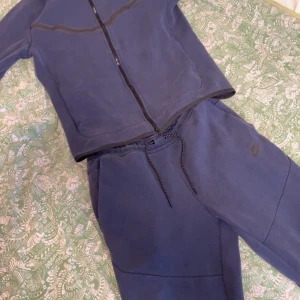 Nike Tech Fleece Set Blå - Säljar mitt mörkblåa Nike tech set då jag inte använder det längre. Byxorna är inte så använda då dem va lite små för mig. Hoodien är däremot använd en del, lite sliten i färgen och har en fläck (sista bilden). Hoodien är i storlek S men är rätt stor i storleken så passar även M. Byxorna är i storlek M. Det går att köpa plaggen var för sig och tillsammans. Priset är inte fast, tar emot bud!