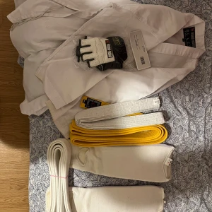 Vit karatedräkt med bälte och handskar - Säljer en vit taekwondo från Budo Nord, tillverkad i 100% bomull. Dräkten kommer med ett vitt och ett gult bälte samt ett par vita handskar. Perfekt för kampsportsträning.