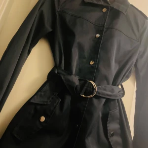 Svart trenchcoat från Zara Basic - Snygg svart trenchcoat från Zara Basic med knappar och bälte i midjan. Jackan har långa ärmar och en klassisk krage. Perfekt för en stilren look.