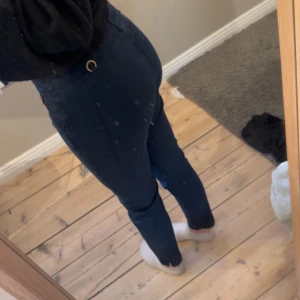 Mörkblå byxor från Stockh LM - Snygga mörkblå byxor från Stockh LM med hög midja och en stilren design. Byxorna har en dekorativ guldringdetalj vid midjan.