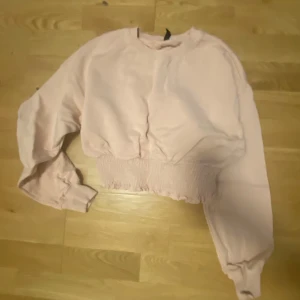 Ljusrosa tröja med resårdetalj - Säljer en ljusrosa tröja med långa ärmar och en unik resårdetalj vid midjan. Perfekt för en avslappnad stil.