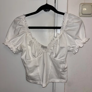 Vit blus med puffärmar - Söt vit blus med puffiga kortärmar och rynkade detaljer vid halsringningen, croppad passform, mjukt och bekvämt material. Endast testad, säljer pga inte rätt passform. Strl 34