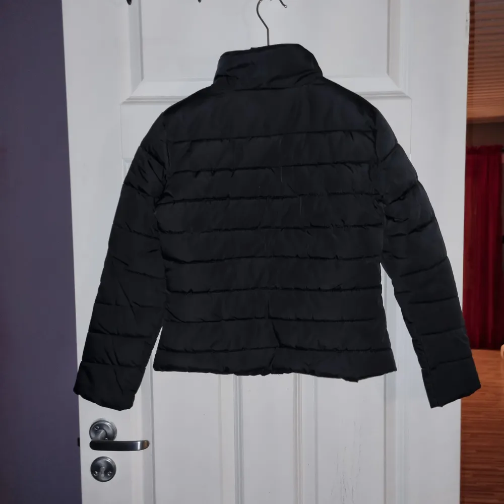 Säljer en stilren svart pufferjacka med dragkedja framtill och två praktiska fickor med dragkedjor. Jackan har en hög krage och är perfekt för kyligare dagar. Den quiltade designen ger en modern look. Nyskick, endast prövad.. Takit.
