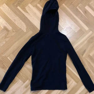Svart hoodie från Hunkydory - Svart tröja med huvud i storlek S. Tröjan är tillverkad i en mjuk bomullsblandning med elastan för extra komfort. Perfekt för en avslappnad look.