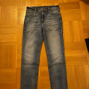 Blå jeans från Lee - Snygga blå jeans från Lee med klassisk femficksdesign och knappgylf. De har en straight passform och är perfekta för en avslappnad stil. Märkeslogga på baksidan och insidan av midjan.