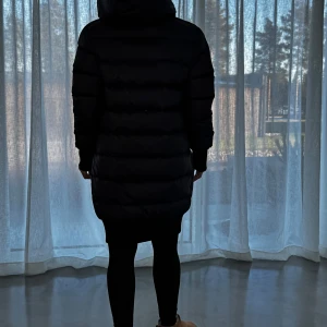 Svart Acne dunjacka med huva - Säljer en stilren Acne 3-in-1 svart dunjacka med huva. Jackan har långa ärmar och stängs med dragkedja och knappar. Perfekt för kyliga dagar.