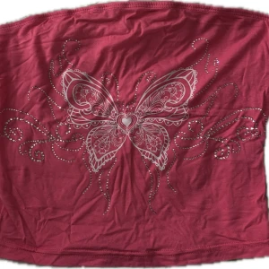 Rosa tubtopp med fjärilsdesign - Snygg rosa tubtopp med en stor vit fjärilsdesign i mitten, dekorerad med glittriga detaljer. Perfekt för att ge en färgglad touch till din outfit.