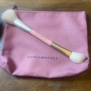 Sminkborste och necessär från Makeup Mekka - Dubbeländad sminkborste med mjuka vita borst och rosa handtag, perfekt för applicering av puder och rouge. Kommer med en matchande rosa necessär i tyg med dragkedja. Använt borsten 2 gånger men har tvättat nessisären helt oanvänd 25 kr för båda