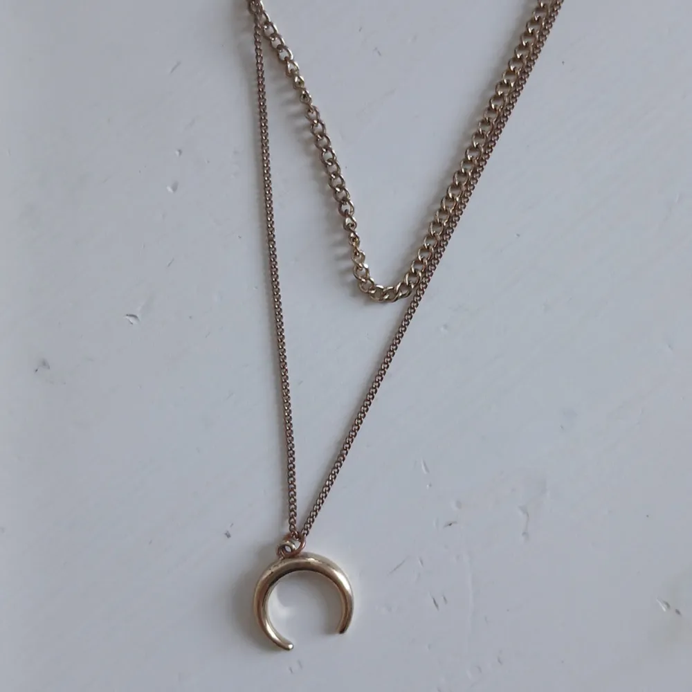 Elegant halsband med två kedjor i guldton. Det ena är en tunn kedja och det andra en grövre kedja. Halsbandet pryds av ett stilrent månhänge som ger en modern touch. Syns lite grann att den är använd men ingen man tänker på. . Asusteet.