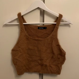 Brun mysig topp - Säljer en brun fluffig topp. Den är ärmlös och har en croppad passform, perfekt för en trendig look. Materialet är mjukt och ger en mysig känsla.