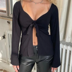Svart långärmad knytblus - Snygg svart långärmad blus med knyt framtill. Perfekt för en stilren look med en djup v-ringning. Passar bra till både jeans och kjol. Tyvärr inte kommit till användning.