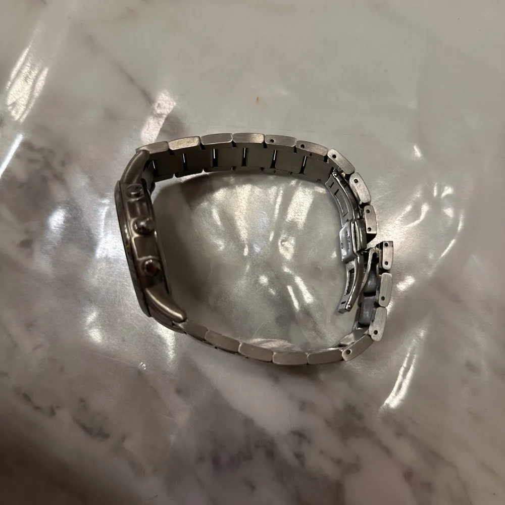 Snygg och stilren klocka från Emporio Armani i silverfärg. Den har en metallarmband och en mörk urtavla med flera små urtavlor för extra funktionalitet. Perfekt för den som vill ha en elegant accessoar.. Asusteet.
