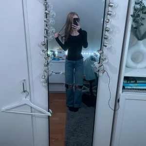 Blå jeans med slitningar - Säljer ett par blå jeans med slitningar vid knäna. De har en straight passform och är högmidjade. Perfekta för en avslappnad stil.