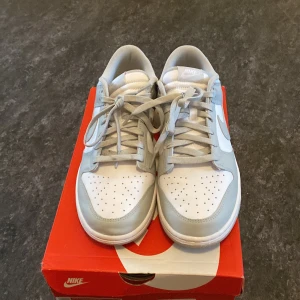 Nike Dunk i vitt och grått - Snygga Nike Dunk sneakers i vitt och grått. Skorna har klassisk snörning och perforerad tå för extra ventilation. Perfekta för en stilren och sportig look. Ny pris 2800