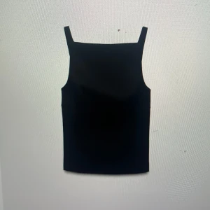 Svart ärmlös topp med rosetter - Snygg svart ärmlös topp med unika rosettdetaljer på baksidan. Toppen har en tight passform och är tillverkad i ett mjukt material. Nypris 380kr, inga defekter!