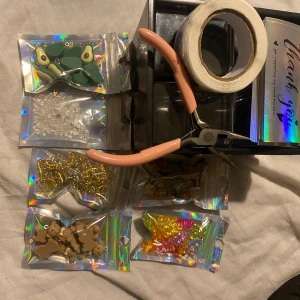 Smyckestillverkningskit med pärlor och verktyg - Ett smyckestillverkningskit som innehåller olika pärlor i form av grodor, björnar och färgglada stjärnor. Kitet inkluderar även ett verktyg med rosa handtag och en rulle med tråd. Perfekt för att skapa egna unika smycken.