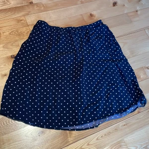 Mörkblå prickig kjol från Holly & Whyte - Säljer en söt mörkblå kjol med vita prickar från Holly & Whyte. Kjolen har en elastisk midja för extra komfort samt fickor i sidorna och är perfekt för en avslappnad stil. Den är lätt och luftig, vilket gör den idealisk för varmare dagar.