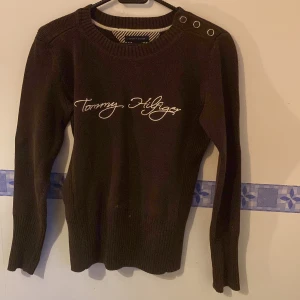 Brun stickad tröja från Tommy Hilfiger - Säljer en snygg brun stickad tröja från Tommy Hilfiger. Den har långa ärmar och en cool detalj med knappar på axeln. Perfekt för höst och vinter, och den är i nyskick. Passar perfekt för en casual look eller när du vill vara lite extra stilren.