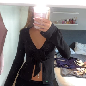 Svart långärmad topp med knyt - Säljer en snygg svart långärmad topp med en stor knytrosett framtill. Toppen har en djup v-ringning och är perfekt för festliga tillfällen. Den är tight och framhäver figuren på ett stilrent sätt.