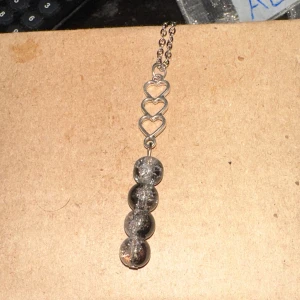 Halsband med hjärtan och glittriga pärlor - Säljer ett unikt halsband med en kedja i silverfärg. Halsbandet har tre små hjärtan i rad och fyra stora glittriga pärlor som hänger nedanför. Perfekt för att ge en extra touch till din outfit!