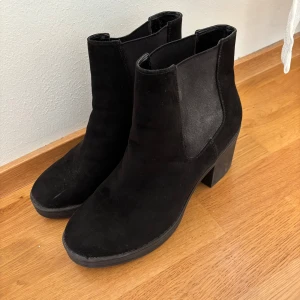 Svarta stövletter i mocka - Säljer ett par snygga svarta stövletter i mocka. De har en bekväm klack och är perfekta för både vardag och fest. Skorna är i bra skick och har en stilren design som passar till det mesta. Perfekta för höst och vinter!