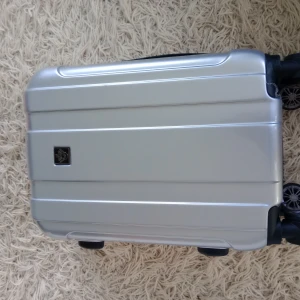 Silverfärgad resväska med hjul - Säljer en snygg och praktisk silverfärgad resväska med fyra hjul för smidig transport. Väskan har en robust design med dragkedja och ett rymligt inre med remmar för att hålla kläderna på plats. Perfekt för resor och weekendresor! Mycket bra skick o oanvänd.