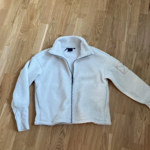 Vit fleecejacka från Didriksons - Mysig vit fleecejacka från Didriksons i storlek 36/38. Perfekt för kyliga dagar med sin mjuka och varma känsla. Jackan har en dragkedja framtill och långa ärmar. Den är i mycket bra skick och passar perfekt för höst och vår. En stilren design med en broderad logga på ärmen.