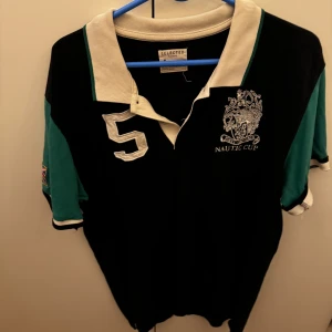 pikétröja från Selected Homme - Säljer en snygg pikétröja från Selected Homme i svart och grönt med vit krage. Den har ett coolt nautiskt märke och siffran 5 på framsidan. Perfekt för en avslappnad stil med en touch av elegans. Passar bra till både jeans och chinos!