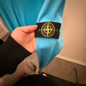 Turkos tröja från Stone Island - Säljer en snygg turkos tröja från Stone Island. Den har en klassisk design med rund hals och långa ärmar. Perfekt för både vardag och festliga tillfällen. Märkesloggan sitter på ärmen för en stilren look. Passar perfekt till jeans eller chinos!
