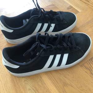 Säljer ett par snygga svarta Adidas sneakers i bra skick. De har den klassiska tre-randiga designen i vitt på sidan och är perfekta för vardagsbruk. Skorna har snörning och en bekväm passform. Perfekta för både vår och höst!