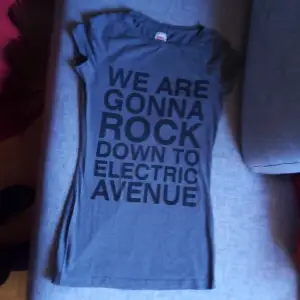 Säljer en grå t-shirt från ONLY i storlek M. Den har ett coolt tryck med texten 'WE ARE GONNA ROCK DOWN TO ELECTRIC AVENUE'. Perfekt för en avslappnad stil eller en konsertkväll. T-shirten är i bra skick och har korta ärmar.