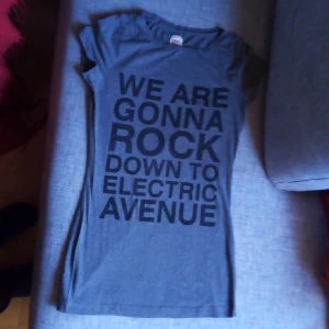Grå t-shirt från ONLY - Säljer en grå t-shirt från ONLY i storlek M. Den har ett coolt tryck med texten 'WE ARE GONNA ROCK DOWN TO ELECTRIC AVENUE'. Perfekt för en avslappnad stil eller en konsertkväll. T-shirten är i bra skick och har korta ärmar.